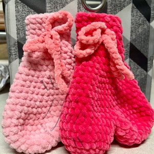 May include: Two crocheted mittens in pink and red with fuzzy yarn. The mittens have a bow detail on the top.