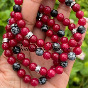 May include: Three stacked bracelets with red and black beads. The bracelets have silver accents and are made of natural stones.