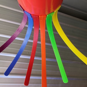 May include: A red, plastic, upside-down cone shape with seven colorful, curved, flat, plastic strips extending downward. The strips are purple, blue, orange, green, and yellow.
