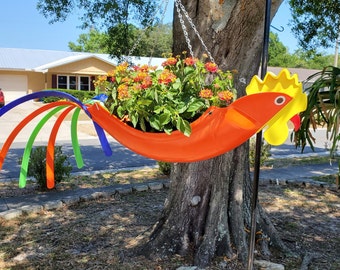 Ollie the Orange Rooster--  yellow crown with a red beak. Bright orange/blue/green tail feathers. Shown with beautiful orange Lantana.