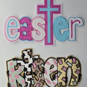 May include: Two embroidered patches, one with the word "easter" in pink, blue, and white sequins and a pink cross, and the other with the word "risen" in a white, pink, and brown fuzzy fabric with a brown cross.