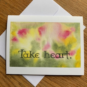 May include: A watercolor greeting card with a yellow, green, and pink abstract background. The card has the text "Take heart." printed in black.