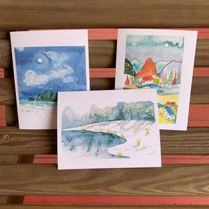 May include: Three watercolor paintings on white card stock. The first painting depicts a blue sky with white clouds and a full moon. The second painting shows a snowy landscape with a river and trees. The third painting features a colorful landscape with mountains, trees, and a boat.