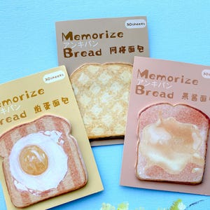 Könnte beinhalten: Drei Notizblöcke mit Brot-Designs. Einer zeigt eine Toastscheibe mit Ei, ein anderer mit Marmelade und der dritte mit einem Gittermuster. Jeder Block hat die Wörter "Memorize" und "Bread" auf Englisch und Japanisch.