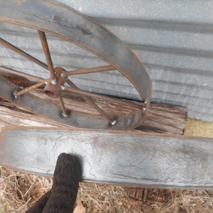 May include: Two metal wheel rims, one with spokes and one without. The rims are rusty and have a grey patina. The rim with spokes is lying on a piece of wood.