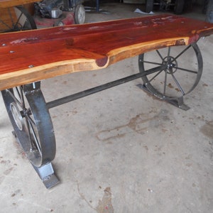 May include: A wooden table with a live edge top and metal wagon wheel legs. The table is made from reclaimed wood and has a rustic look.