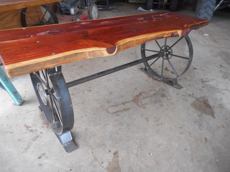 May include: A wooden table with a live edge top and metal wagon wheel legs. The table is made from reclaimed wood and has a rustic look.