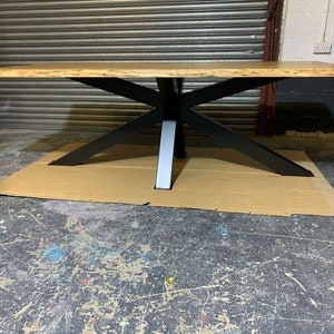 May include: A large wooden table with a live edge top and a black metal base. The table is sitting on a brown cardboard surface.