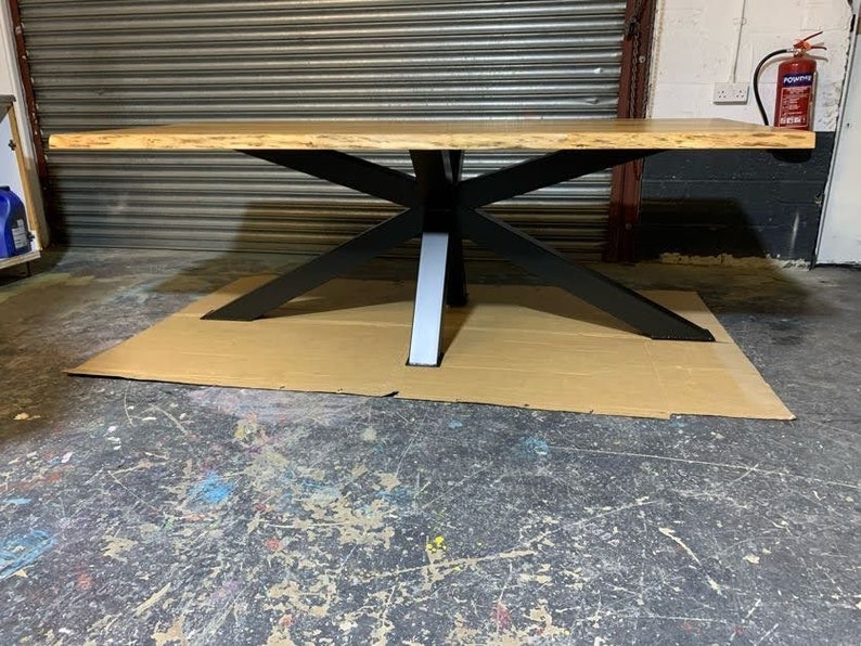 May include: A large wooden table with a live edge top and a black metal base. The table is sitting on a brown cardboard surface.