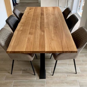 May include: A large wooden dining table with a live edge design. The table has a natural wood finish and is supported by a black metal base. Six chairs with brown upholstery surround the table.