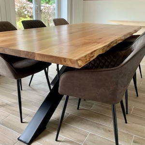 May include: A large wooden dining table with a live edge top and a black metal X-shaped base. The table is surrounded by six brown upholstered chairs with black metal legs.