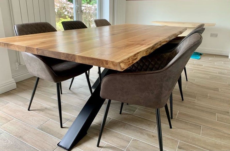 May include: A large wooden dining table with a live edge top and a black metal X-shaped base. The table is surrounded by six brown upholstered chairs with black metal legs.