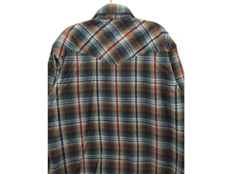 May include: A long-sleeved button-up shirt featuring a plaid pattern in shades of brown, dark green, blue, and red. The shirt has a pointed western-style back yoke and a standard collar, showcasing a textured fabric finish throughout the garment.