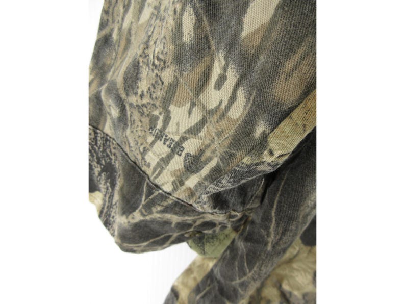 Puede incluir: Primer plano de una tela de camuflaje. La tela presenta una mezcla de tonos verdes, marrones y beige, creando un dise&ntilde;o naturalista. La palabra "BEARUP" es visible en la tela.