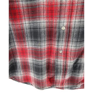 May include: A long-sleeved button-down shirt featuring a plaid pattern in shades of red, black, and grey. The garment includes a front placket with two visible silver-toned metal snap buttons and a soft, textured fabric finish throughout the piece.
