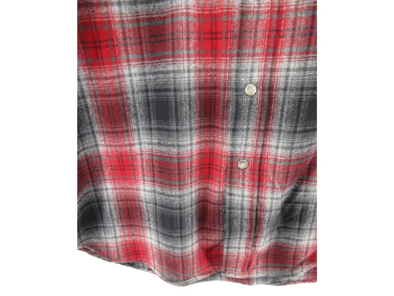 May include: A long-sleeved button-down shirt featuring a plaid pattern in shades of red, black, and grey. The garment includes a front placket with two visible silver-toned metal snap buttons and a soft, textured fabric finish throughout the piece.