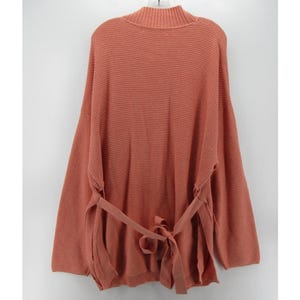 May include: A coral-colored knit sweater with a mock neck and long sleeves. The sweater features a tie belt at the waist and a textured knit pattern. The back view of the sweater is shown.