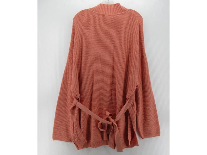 May include: A coral-colored knit sweater with a mock neck and long sleeves. The sweater features a tie belt at the waist and a textured knit pattern. The back view of the sweater is shown.