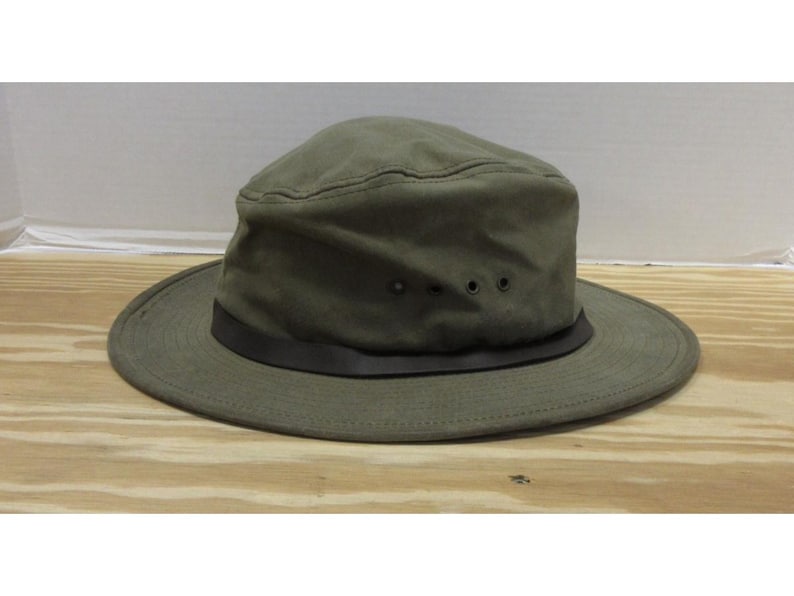 Op de afbeelding: Olijfgroene hoed met een brede rand en een donkerbruine band. De hoed heeft een gestructureerde kroon met drie kleine ventilatiegaten. Gemaakt van duurzame stof, geschikt voor buitenactiviteiten.