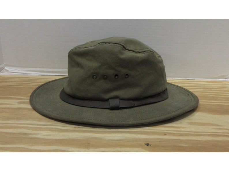 Op de afbeelding: Olijfgroene hoed met een brede rand en een donkerbruine band. De hoed heeft een gestructureerde kroon met ventilatie-ogen. Een casual outdoor accessoire.