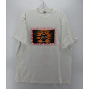 Może przedstawiać: Biała koszulka z czarno-pomarańczową grafiką zespołu "Black Sabbath" z tekstem "It Ain't Safe Anymore".