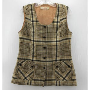 May include: A vintage plaid vest in tan, black, and cream. The vest has a button-up front, two front pockets, and a brown lining. The sleeveless vest hangs on a clear hanger. The plaid pattern is a classic design.