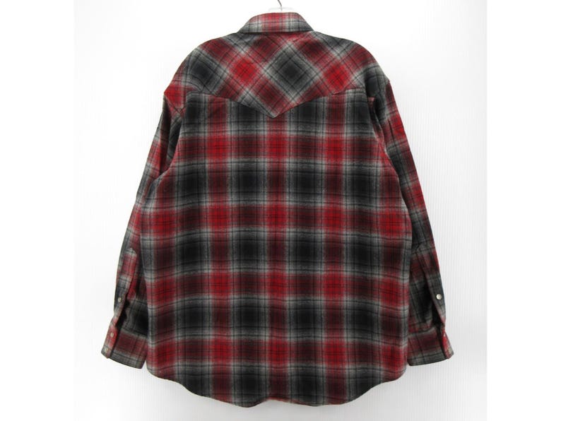 May include: A long-sleeve button-down shirt featuring a red, black, and grey plaid pattern. The shirt has a pointed collar, a western-style back yoke, and cuffs with button closures. The fabric displays a soft, brushed texture throughout the garment.