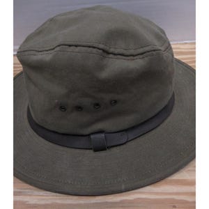 Op de afbeelding: Olijfgroene hoed met een zwarte band en rand. De hoed heeft een gestructureerde kroon met een gestikte naad en drie ventilatiegaten. Een zwarte leren riem is aan de band bevestigd.