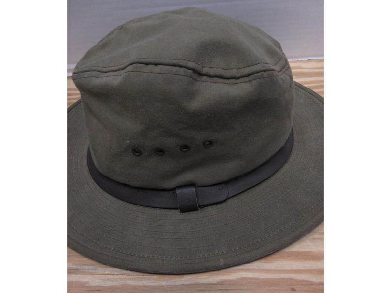 Op de afbeelding: Olijfgroene hoed met een zwarte band en rand. De hoed heeft een gestructureerde kroon met een gestikte naad en drie ventilatiegaten. Een zwarte leren riem is aan de band bevestigd.