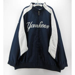 May include: Navy blue Yankees jacket with white accents on the shoulders and sleeves. The word "Yankees" is embroidered across the chest in white script. The jacket has a full zipper and a black hem and cuffs.