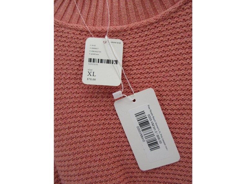 May include: Close-up of a coral-colored knit sweater. The sweater has a textured pattern and a round neckline. Attached tags indicate size XL.