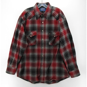 May include: A long-sleeved button-down shirt featuring a red, black and grey plaid pattern. The shirt includes a pointed collar, two chest pockets with buttoned flaps, and metallic snap buttons running down the front placket and on the cuffs.