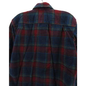 May include: A long-sleeve button-down shirt featuring a plaid pattern in shades of dark red, navy blue, and forest green. The shirt has a standard collar, a back yoke with a central box pleat, and long sleeves with buttoned cuffs.