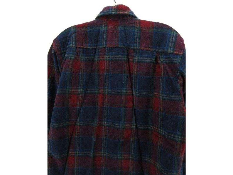 May include: A long-sleeve button-down shirt featuring a plaid pattern in shades of dark red, navy blue, and forest green. The shirt has a standard collar, a back yoke with a central box pleat, and long sleeves with buttoned cuffs.