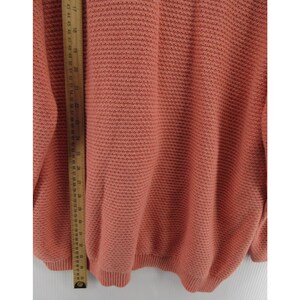 May include: A coral-colored sweater with a textured knit pattern. The sweater has a ribbed hem and cuffs. A wooden ruler is placed vertically along the side of the sweater, showing measurements in inches.