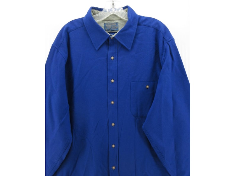 May include: A long-sleeved button-down shirt in a vibrant royal blue color. The shirt features a classic collar, a single chest pocket on the left side, and light-colored buttons down the front placket. The interior collar lining is a light gray.