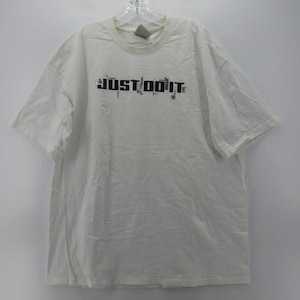 May include: A white short-sleeved t-shirt with the text "JUST DO IT" in black, with a gray Nike logo on the upper chest. The shirt is hanging on a clear hanger against a white background.