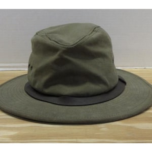 Op de afbeelding: Olijfgroene hoed met een brede rand en een donkerbruine band. De hoed heeft een gestructureerde kroon en lijkt gemaakt te zijn van een duurzame stof. Een praktisch accessoire voor bescherming tegen de zon en buitenactiviteiten.