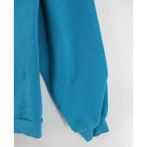May include: A solid teal long-sleeve sweatshirt featuring a crew neckline and ribbed cuffs at the wrists. The garment is constructed from a soft, fleece-like fabric and displays a plain, unpatterned design with a consistent vibrant blue-green color.