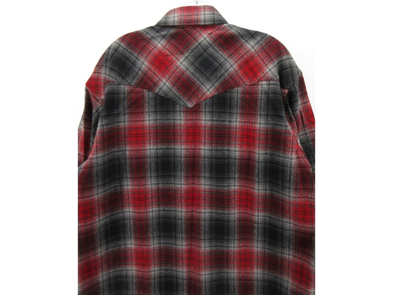 May include: A long-sleeve button-up shirt featuring a red, black, and grey plaid pattern. The garment includes a pointed back yoke design, a standard collar, and a textured fabric finish, showcasing a consistent checkered print throughout the back.