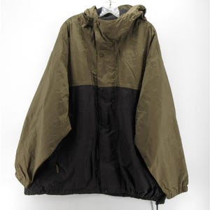 Puede incluir: Una chaqueta con capucha de dos tonos que presenta una sección superior de color verde oliva y una sección inferior negra. La chaqueta incluye un cierre de cremallera frontal, un cuello alto y mangas largas con puños elásticos.