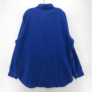 May include: A solid royal blue long-sleeve button-down shirt featuring a standard collar, a back yoke, and cuffs with buttons. The garment is displayed from the back view, showcasing the plain fabric texture and the structured cut of the shirt.