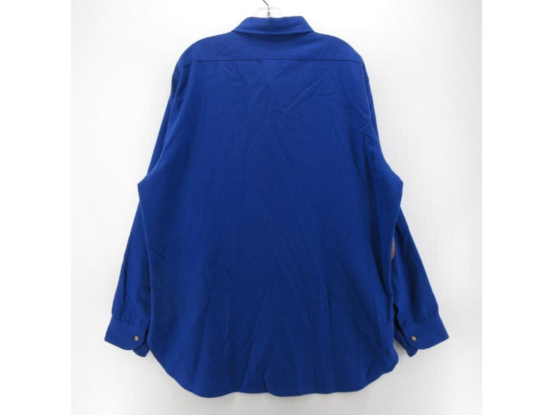 May include: A solid royal blue long-sleeve button-down shirt featuring a standard collar, a back yoke, and cuffs with buttons. The garment is displayed from the back view, showcasing the plain fabric texture and the structured cut of the shirt.