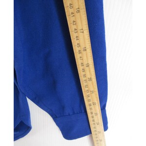 May include: A solid royal blue long-sleeved shirt with a buttoned cuff. A wooden ruler is placed vertically along the sleeve, showing a measurement of approximately 25 inches from the shoulder seam to the end of the cuff.
