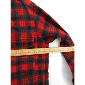 Puede incluir: Una camisa de franela de manga larga con un patr&oacute;n de cuadros en rojo, negro y verde oscuro, que incluye un bolsillo en el pecho con bot&oacute;n. Una regla de madera colocada sobre la parte central muestra una medida de unos 28 cent&iacute;metros.