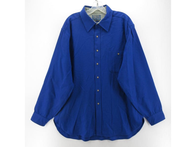 May include: A long-sleeve button-down shirt in a solid royal blue color. The shirt features a classic collar, a single chest pocket on the left side, and a full-length front button placket with matching blue buttons. The interior collar lining is light gray.
