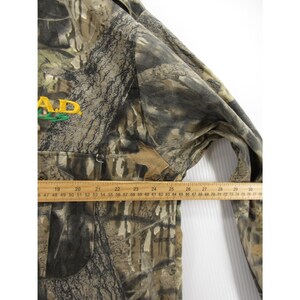 Puede incluir: Chaqueta con estampado de camuflaje con el texto "A.D." en bordado amarillo y verde. La chaqueta tiene una cremallera y una regla colocada en la parte delantera, que mide en cent&iacute;metros.