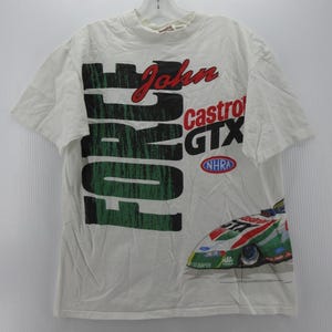 May include: A white short-sleeve t-shirt featuring large black and green text that reads John Force. The shirt includes red text reading Castrol GTX, an NHRA logo, and a graphic of a race car with green, red, and white paint on the lower right side.