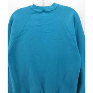 May include: A solid teal sweatshirt featuring a crew neckline and long raglan sleeves. The garment is constructed with a ribbed collar and cuffs, showcasing a plain, unpatterned design throughout the front and back of the fabric.