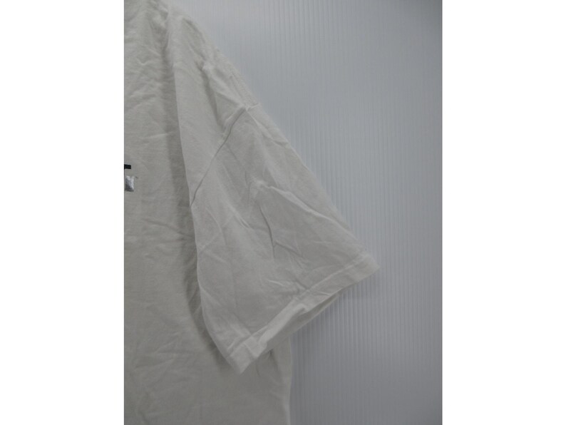 May include: A white short-sleeved t-shirt with a visible logo on the front. The shirt is made of a soft, slightly wrinkled fabric. The sleeve is visible in the image.